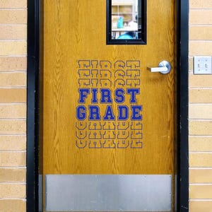 Puede incluir: Una puerta de madera con las palabras "FIRST GRADE" en letras azules. La puerta tiene una placa protectora plateada y una pequeña ventana en la parte superior. La puerta está enmarcada en negro y rodeada por una pared de ladrillos.