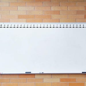 May include: A white whiteboard with a black number line from -13 to 18. The whiteboard is mounted on a brick wall. A black eraser and a red marker are on the whiteboard.