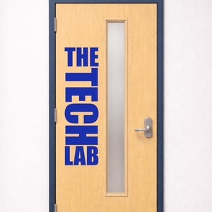 May include: A closed wooden door with a rectangular glass panel and the words "THE TECH LAB" in blue. The door has a silver handle and a metal kick plate. The door frame is dark blue, and the wall is white.