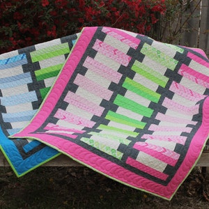 Può includere: Due quilt con un design a patchwork in tessuto rosa, verde, blu, bianco e grigio. Le quilt sono piegate ed esposte su una panca di legno.