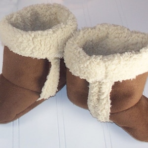 May include: A pair of brown suede slipper boots with a white faux fur lining. The boots have a fold-over cuff and are perfect for keeping your feet warm in the winter.