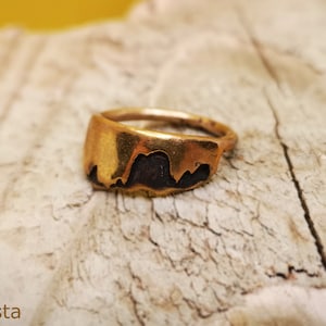 Op de afbeelding: Een ring van goudkleurig metaal met een uniek, abstract ontwerp. De ring heeft een getextureerd oppervlak.