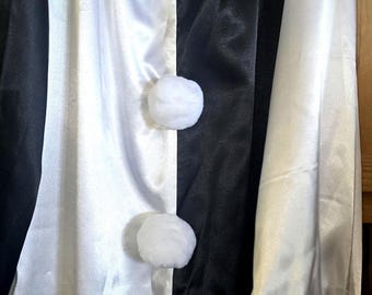 May include: A black and white clown costume made of satin-like fabric. The costume features a ruffled collar, long sleeves, and white pom-pom buttons. The design is split vertically, with one side white and the other black.