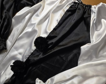 May include: A black and white satin clown costume with long sleeves and pom-pom accents. The costume features alternating panels of black and white fabric, with a ruffled neckline and cuffs. The clown costume is designed for a festive occasion.