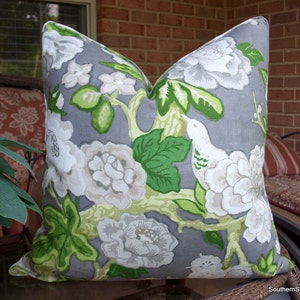 May include: A gray pillow with a floral pattern featuring white flowers, green leaves, and a white bird. The pillow has a light gray background and is made of a soft, comfortable fabric.