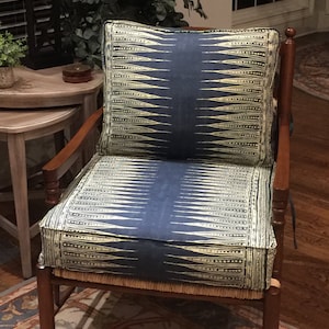 May include: A wooden armchair with a blue and yellow patterned cushion. The chair has a woven cane seat and a dark wood frame.