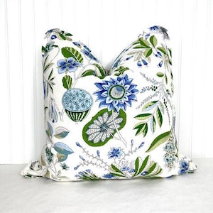 May include: A white pillow cover with a blue and green floral pattern. The pattern features large blue flowers, green leaves, and small blue flowers.