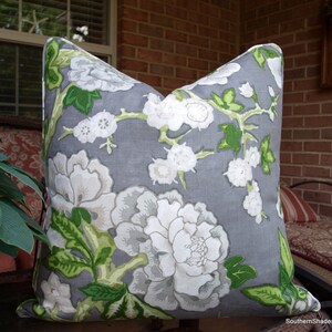 May include: A gray pillow with a floral pattern featuring white flowers, green leaves, and gray branches. The pillow is made of a soft, textured fabric.