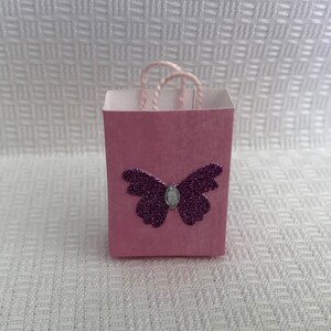 May include: A small pink gift bag with a purple glitter butterfly design.