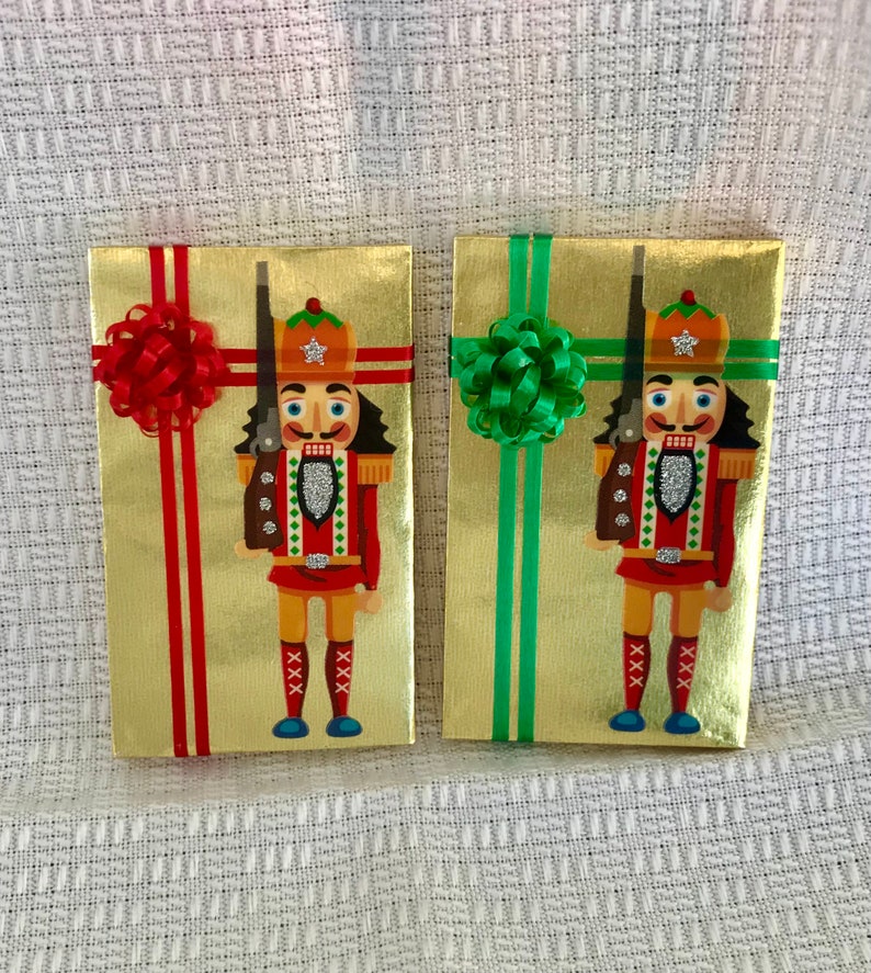 May include: Two gold gift boxes with nutcracker designs. One box has a red bow and the other has a green bow.