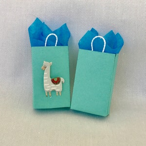 May include: Two light blue gift bags with white handles. One bag features a white llama with a colourful saddle.