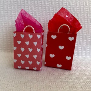 May include: Two small gift bags with white heart patterns. One bag is red and the other is pink.
