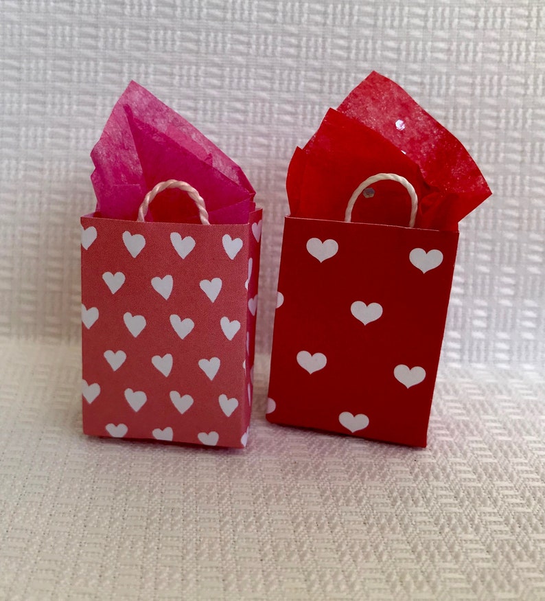 May include: Two small gift bags with white heart patterns. One bag is red and the other is pink.