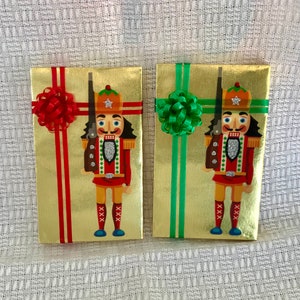 May include: Two gold gift boxes with nutcracker designs. One box has a red bow and the other has a green bow.