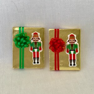 May include: Two gold gift boxes with nutcracker designs. One box has a green bow and the other has a red bow.