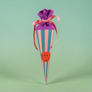 Può includere: Un sacchetto regalo a forma di cono colorato con un adesivo a forma di faccina sorridente. La borsa presenta strisce turchesi e corallo alternate, una parte superiore viola e un nastro rosa. Per piccoli regali o dolcetti.