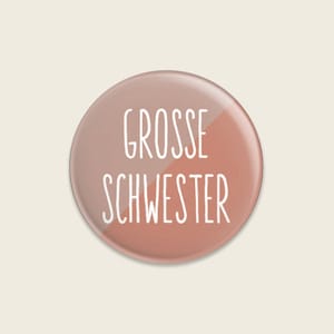 May include: A round button with a pink and peach gradient background. The text "Grosse Schwester" is written in white on the button.