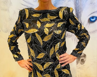 Puede incluir: Una blusa negra de manga larga con un estampado de hojas doradas y negras. La blusa está hecha de una tela transparente y está cubierta de lentejuelas.
