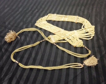 May include: A beige beaded belt with a tassel on each end. The belt is made of multiple strands of beads and has a simple design.