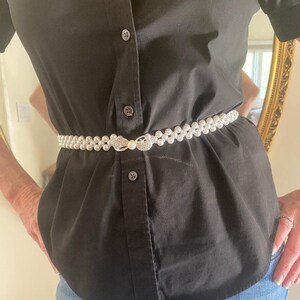 May include: A black button-down shirt with a pearl and rhinestone belt. The shirt is tucked into blue jeans.