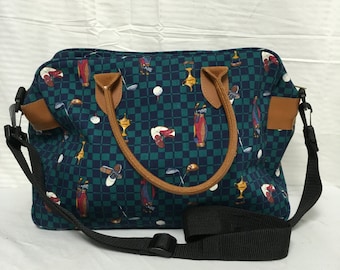 May include: A blue and brown golf-themed tote bag with a checkered pattern and a black adjustable shoulder strap.