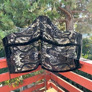May include: A black velvet shawl with a gold paisley pattern. The shawl is draped over a metal stand and is hanging on a wooden railing.