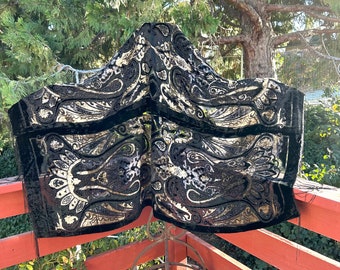 May include: A black velvet shawl with a gold paisley pattern. The shawl is draped over a metal stand and is hanging on a wooden railing.