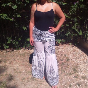 May include: A woman wearing a black tank top and white pants with a black and white paisley pattern. The pants have a wide leg and a ruffled hem.