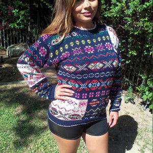 May include: A woman wearing a blue, red, white, and pink patterned sweater with a black and white geometric design. She is also wearing black shorts.