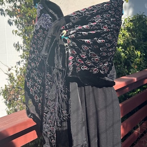 May include: Black shawl with a velvet texture and a peacock feather pattern in red and white. The shawl is draped over a black dress form. The shawl has a fringe detail and a peacock brooch.