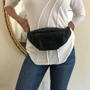 May include: A black leather fanny pack with a zippered pocket and adjustable buckle closure.