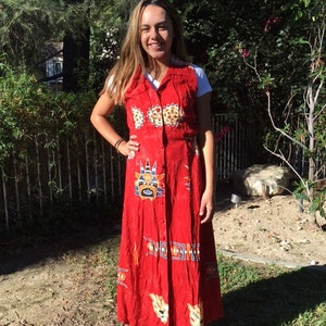 May include: A red maxi dress with a sleeveless bodice and a button-up front. The dress features a colourful, geometric pattern with animal faces and tribal designs.