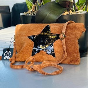 May include: A brown suede crossbody bag with a large star-shaped sequin embellishment. The bag has a brown leather strap and a small black tag with the text "ÉFFE" on it.