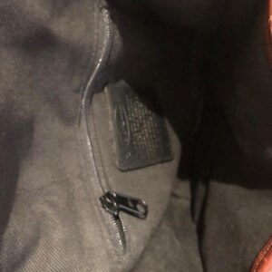 Op de afbeelding: De binnenkant van een bruine leren tas met een ritsvak en een zwart leren label. Het label heeft de tekst "Fossil" erop gedrukt.