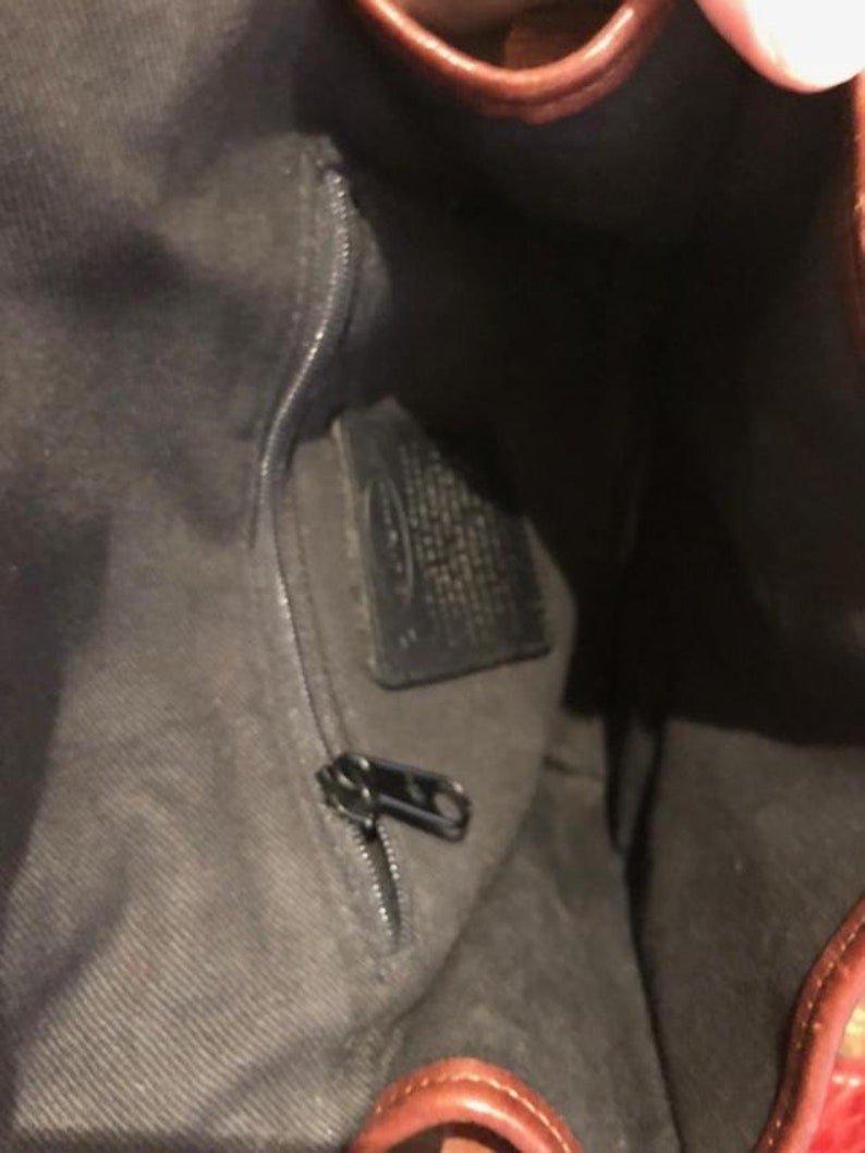 Op de afbeelding: De binnenkant van een bruine leren tas met een ritsvak en een zwart leren label. Het label heeft de tekst "Fossil" erop gedrukt.