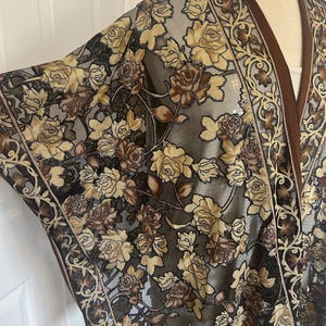 Pode incluir: Um xale marrom transparente com um padrão floral de rosas douradas e marrons. O xale tem uma borda de franjas.