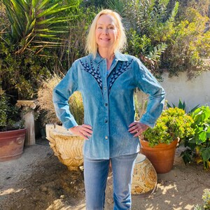 Könnte beinhalten: Eine Frau trägt ein hellblaues Jeanshemd mit einem schwarz-weißen geometrischen Muster auf der Vorderseite. Sie trägt eine blaue Jeans und steht in einem Garten.