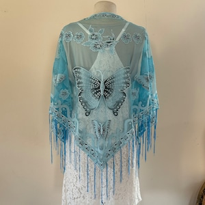 May include: A light blue sheer shawl with a butterfly design and fringe trim. The shawl is decorated with floral accents and has a delicate lace pattern.