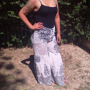 May include: White pants with a black and white paisley print. The pants have a wide leg and a ruffled hem.
