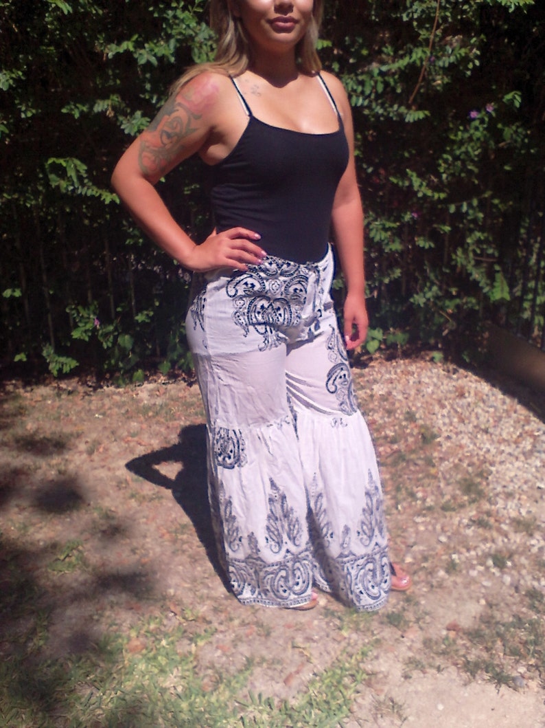 May include: White pants with a black and white paisley print. The pants have a wide leg and a ruffled hem.