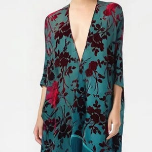 May include: A teal floral kimono with a deep V-neck and three-quarter sleeves. The kimono features a dark red floral pattern and teal fringe along the bottom hem. The garment is made of a lightweight, flowing fabric.