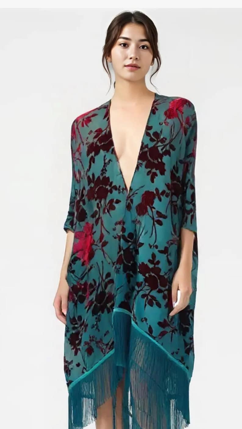May include: A teal floral kimono with a deep V-neck and three-quarter sleeves. The kimono features a dark red floral pattern and teal fringe along the bottom hem. The garment is made of a lightweight, flowing fabric.