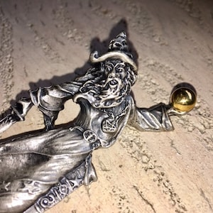 Pode incluir: Uma figura de prata de um mago usando um chapéu pontudo e segurando um orbe dourado na mão direita.