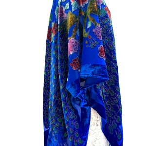 May include: A royal blue velvet shawl with a peacock feather design and floral embroidery. The shawl has a fringe trim and is draped over a white dress form.