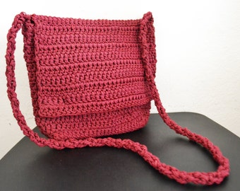 May include: A burgundy crocheted shoulder bag with a long strap. The bag is made of a thick, textured yarn and has a simple, classic design.