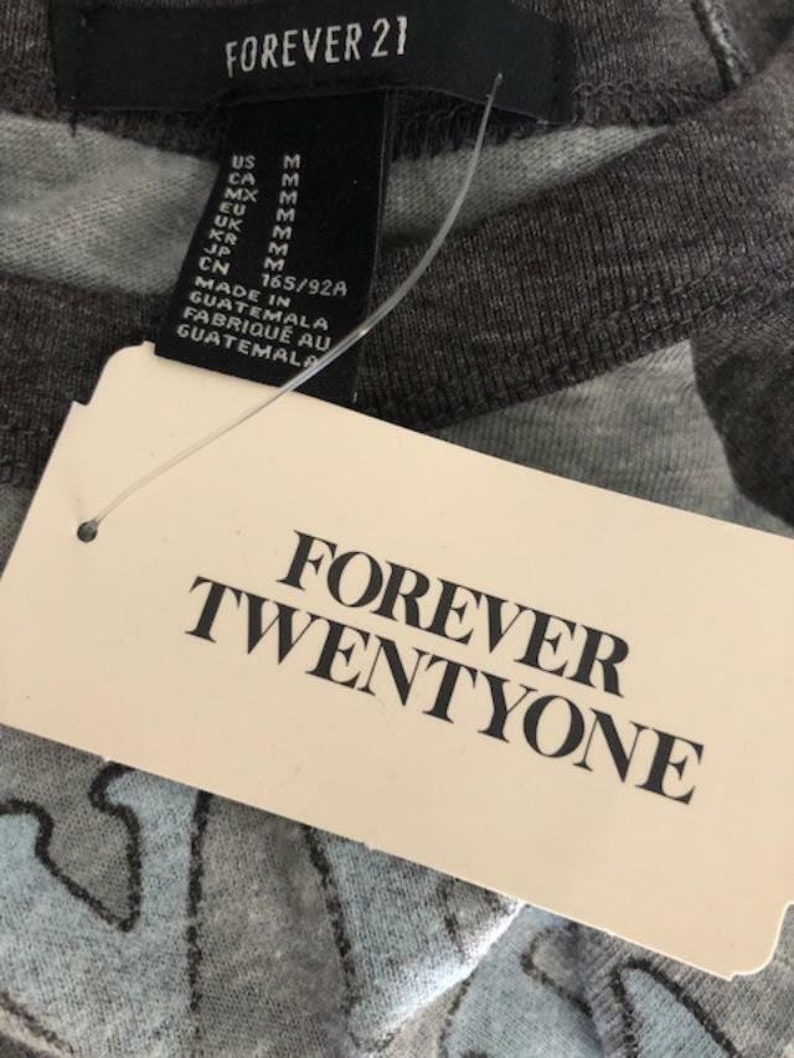 May include: Close-up of a gray Forever 21 t-shirt tag with the brand name and size information. The tag reads "FOREVER TWENTYONE" in bold black letters. The shirt has a light blue and gray pattern.