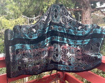 May include: A black velvet shawl with a teal and silver paisley pattern. The shawl has a fringed edge and is draped over a metal stand.