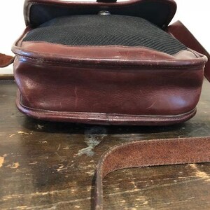 Op de afbeelding: Een bruine leren schoudertas met een zwarte canvas klep en een bruine leren riem.