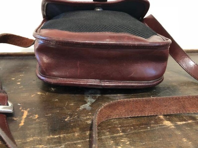 Op de afbeelding: Een bruine leren schoudertas met een zwarte canvas klep en een bruine leren riem.