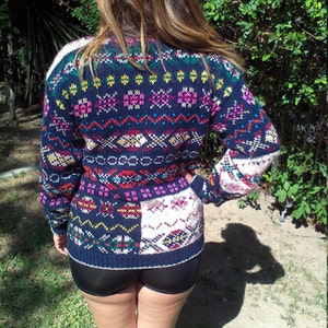 May include: A colorful knitted sweater with a geometric pattern in shades of blue, pink, yellow, and white. The sweater has a loose fit and a crew neck.
